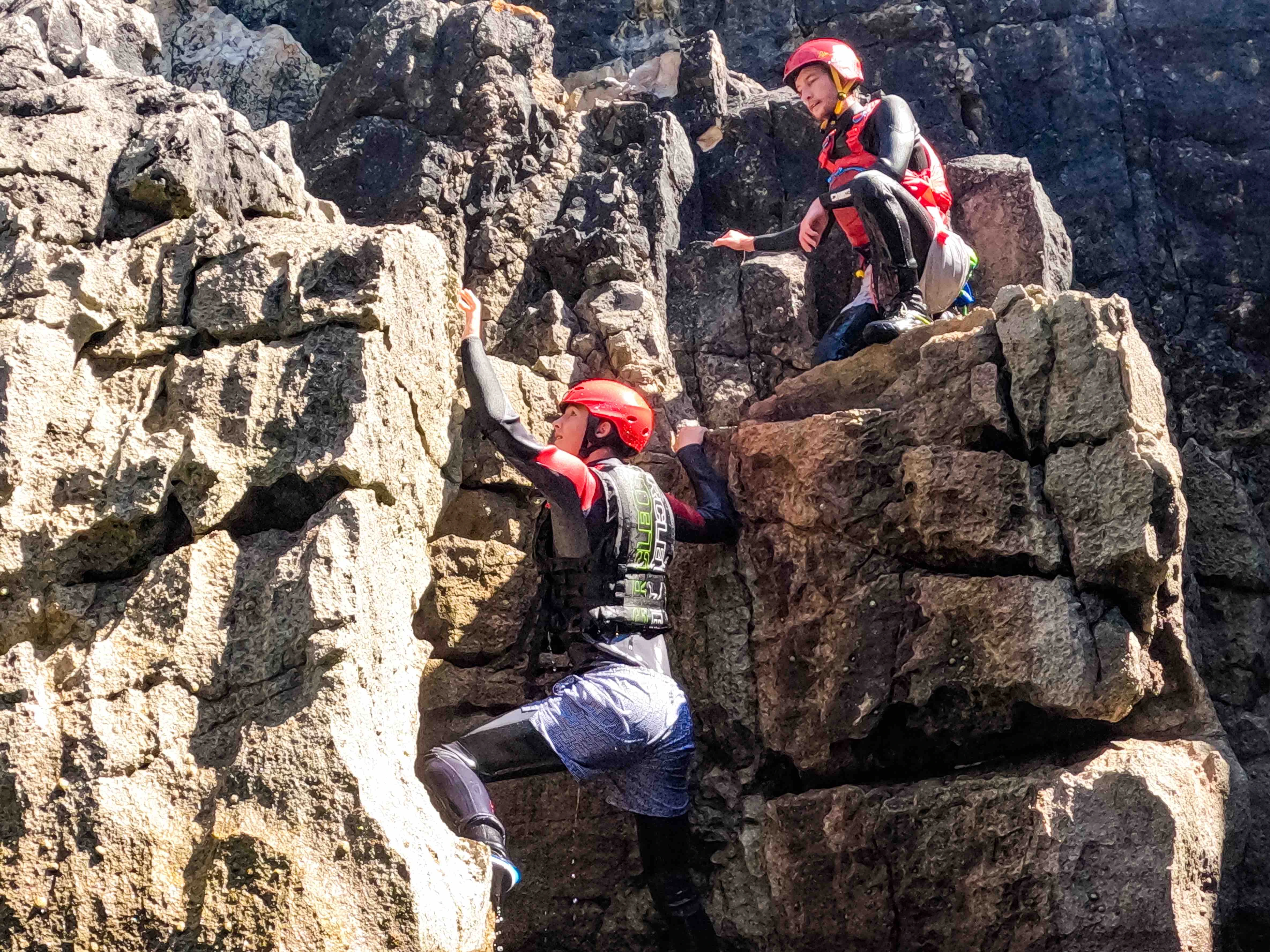 An instructor from Pembrokeshire Coastal Adventure is guiding a client to climb rocks.